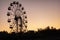 Silhouette of a ferris wheel at sunrise sunset of the sun on a background of trees and grass