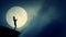 Silhouette figure holding hands in prayer on a cliff in a rising full moon night