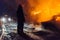 Silhouette of a firefighter in protective suit standing against the fire at night