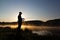 Silhouette of the fisherman at dawn catching fish in the river. Cold summer morning and mist over the river.