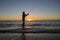 Silhouette of fisherman with hat on the beach with fish rod standing on sea water fishing at sunset with beautiful orange sky in v