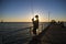 Silhouette of fisherman with hat and fish rod standing on sea dock fishing at sunset with beautiful orange sky in vacations relax