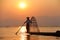 Silhouette of a fisherman near lake catching fish in a traditional way with a handmade net at sunset