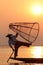 Silhouette of a fisherman near lake catching fish in a traditional way with a handmade net at sunset