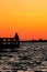 Silhouette of a fisherman standing alone on a fishing pier under a vibrant sunset sky