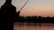 Silhouette fisherman throwing fishing rod in river on background evening sunset