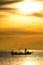 Silhouette of fishermen in the boat on sea with yellow and orange sun in the background