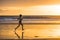 Silhouette of fit and athletic Asian Chinese sporty woman running on beautiful beach doing jogging workout on sunset in fitness he