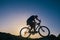 Silhouette of a fit male mountain biker riding his bike uphill on rocky harsh terrain on a sunset