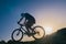 Silhouette of a fit male mountain biker riding his bike uphill on rocky harsh terrain on a sunset