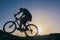 Silhouette of a fit male mountain biker riding his bike uphill on rocky harsh terrain on a sunset