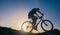 Silhouette of a fit male mountain biker riding his bike uphill on rocky harsh terrain on a sunset