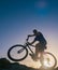 Silhouette of a fit male mountain biker riding his bike uphill on rocky harsh terrain on a sunset