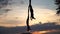 Silhouette of Flexible female acrobat doing crazy and dangerous trick with red aerial silk on the sunset sky background