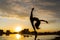 Silhouette Flexible female dancer making trick with reflection in the water during dramatic sunset. Concept of happiness