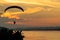 Silhouette flying paramotor over river and sunset sky
