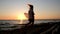 Silhouette of a free girl in a white shirt walking along the seashore in the sunset