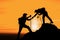 Silhouette of friend helping friend climbing up mountain by giving a hand