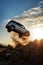 silhouette of a generic silver car crashing flying off a cliff. Stone cliff. Blue sunset sky. White warm clouds. Car accident.