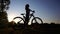 Silhouette of girl cyclist with ponytail hairstyle walking with her bike. Slow motion shot against sunset