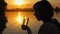 Silhouette of girl drinking water from glass by the river at sunset, slow motion