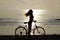 Silhouette of a girl with long hair on a bicycle riding on the sand by the Baltic sea. Shooting against the sun