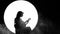 Silhouette of a girl-musician. A young woman plays on an acoustic guitar sitting on a white circle background as a full moon in th