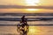 Silhouette of a girl riding tricycle on a beach in a starting tide