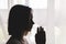 Silhouette of girl at window of clasped hand in gesture of prayer.