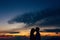 Silhouette of groom in the hat kisses bride on the forehead at sunset