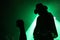 Silhouette of a guitarist on stage with a cowboy hat with fan\'s fist in front of green reflector