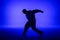 Silhouette of guy in casual clothes dancing elements of hip hop in studio with blue light. Dancer demonstrates body