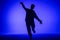 Silhouette of guy in casual clothes dancing elements of hip hop in studio with blue light. Dancer demonstrates body