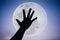 Silhouette of a hand with large full moon on fantastic sky background.