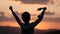 Silhouette of happy champion little boy child holding up golden medal in hand