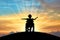 Silhouette of a happy disabled child girl sitting in a wheelchair atop a hill at sunset