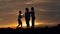 Silhouette of happy family father of mother and two sons playing outdoors in field at sunset
