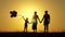 Silhouette of a happy family at sunset. Dad, mom and baby hold hands and look at each other. A little boy holds balloons