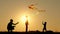 Silhouette of a happy family at sunset. Father and two sons fly a kite in the background of bright sun. Rest and play in