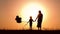 Silhouette of a happy family at sunset. A mother and a child with balloons hold each other`s hands. Beautiful orange background