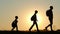 Silhouette of a happy family of tourists go with backpacks, during sunset. Dad and two sons are following each other.