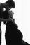 Silhouette of happy husband kissing his pregnant wife in stylish black dress and holding belly bump in light. Fashionable pregnant