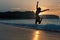 Silhouette of happy joyful woman jumping and having fun at the beach against the sunset. Freedom and leisure vacation concept.