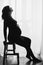 Silhouette of happy pregnant woman in stylish black dress sitting on ladder and holding belly bump in light. Fashionable pregnant