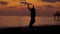 Silhouette of happy slim woman is jumping on a sea coast in evening time after sunset and rising hands