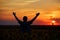 Silhouette of happy successful corn farmer in cornfield in sunset with arms raised in the air