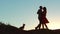 Silhouette of a happy young married couple and dog slow dancing outside at sunset. slow motion video. man and girl