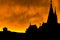 Silhouette of a Harlem rooftop, chimneys, and church steeples, against a bright yellow fiery-looking sky during sunset