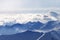 Silhouette of high snowy mountains in mist and sunlit cloudy sky at winter