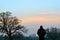 A silhouette of a hooded figure standing in a field, watching the sunset on a winters afternoon.